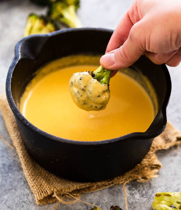 Black Cast Iron Skillet Filled with creamy cheese sauce with a hand dipping broccoli into it.