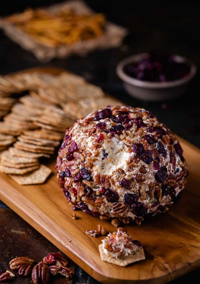 Cheese ball covered in dried cranberries and pecans on a wooden cutting board with crackers