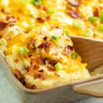 Twice baked potato casserole in a casserole dish with a wooden spoon scooping it up.