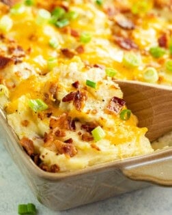 Twice baked potato casserole in a casserole dish with a wooden spoon scooping it up.