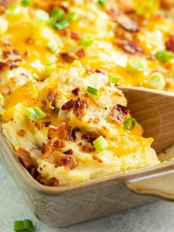 Twice baked potato casserole in a casserole dish with a wooden spoon scooping it up.