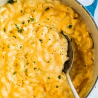 A spoon scooping up creamy Mac and Cheese from a Dutch oven.