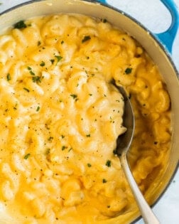 A spoon scooping up creamy Mac and Cheese from a Dutch oven.