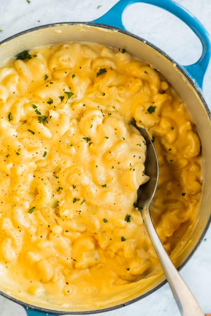 Overhead Shot of a big pot full of creamy macaroni and cheese with a spoon scooping it out of the pot. 