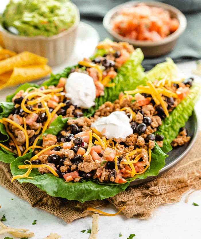 Turkey Taco Lettuce Wraps on a plate with sour cream on top and guacamole and salsa in the background.