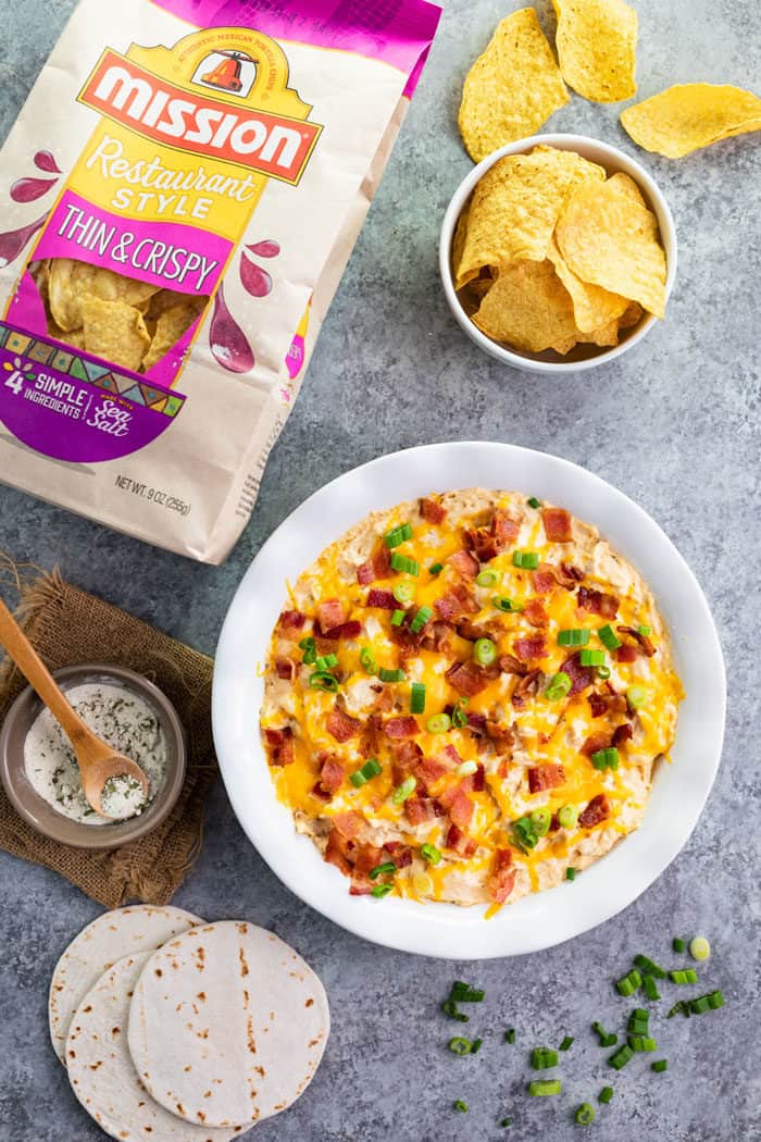 Overhead shot of a bowl of chicken ranch bacon dip in a white bowl surrounded by tortilla chips.