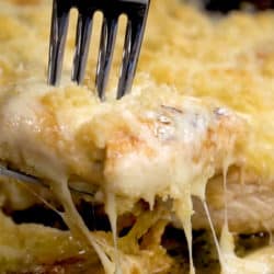 A fork pulling up cheesy Parmesan crusted chicken from a pan.