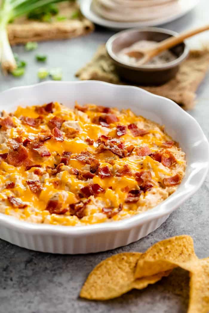 White bowl with chicken ranch bacon dip with tortilla chips in front.