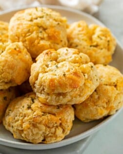 A white plate with a pile of Cheddar Bay Biscuits with parsley on top.