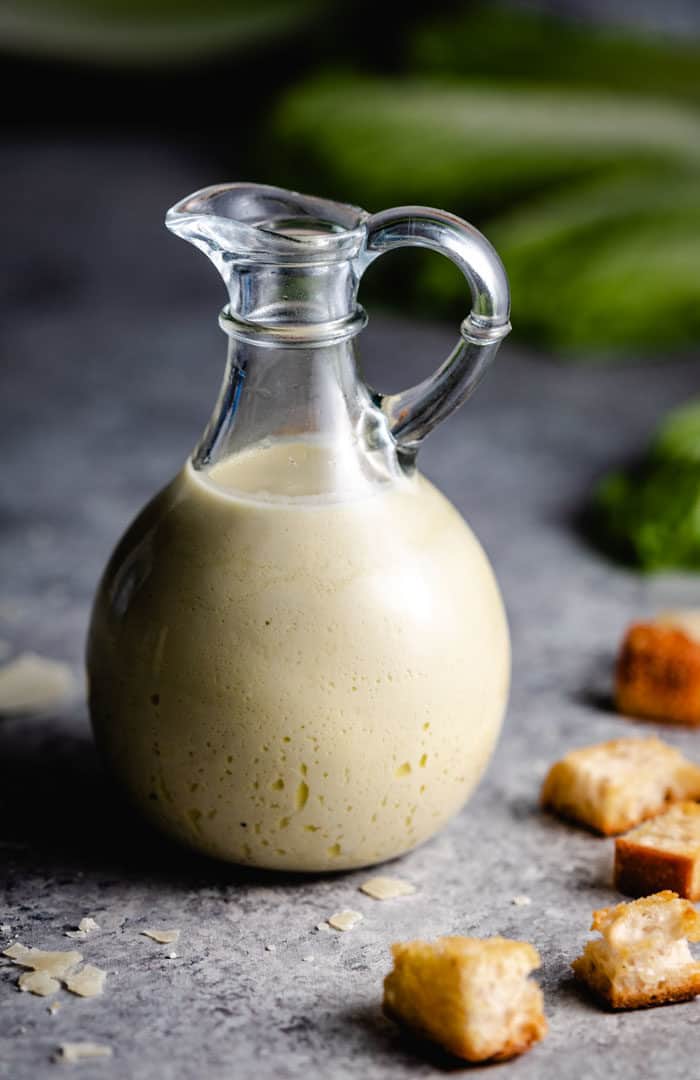 A bottle of Caesar salad dressing on a blue surface with croutons next to it.