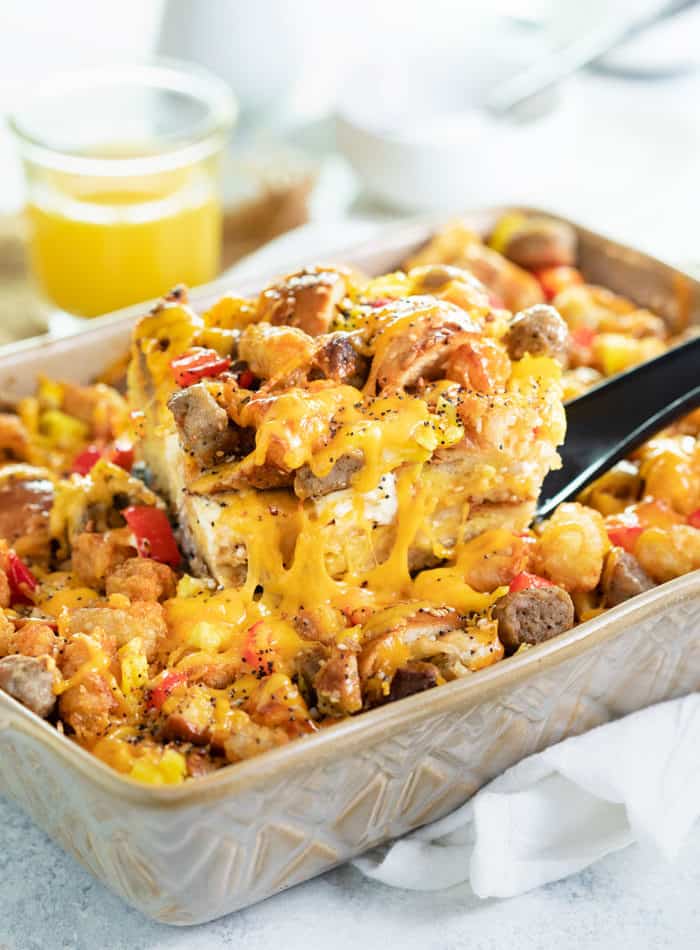 A spatula pulling up a slice of everything bagel breakfast casserole from casserole dish with orange juice in background.