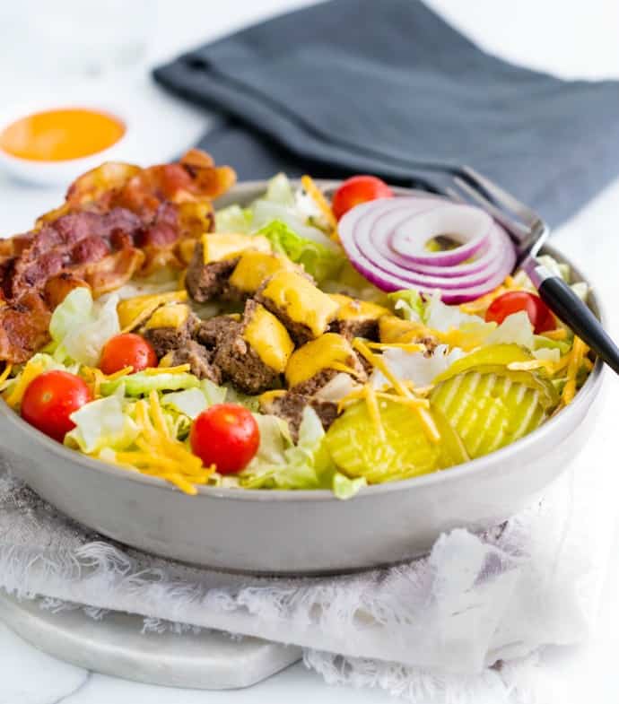 A big gray bowl filled with cheeseburger salad with big mac sauce and a dish towel in the background.