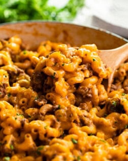 A skillet with a wooden spoon scooping up Cheeseburger Casserole