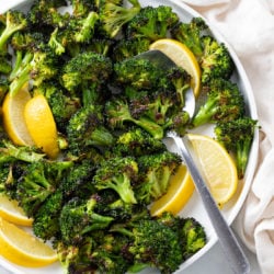 A white plate with roasted broccoli and slices of lemon with a spoon.