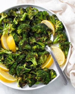 A white plate with roasted broccoli and slices of lemon with a spoon.