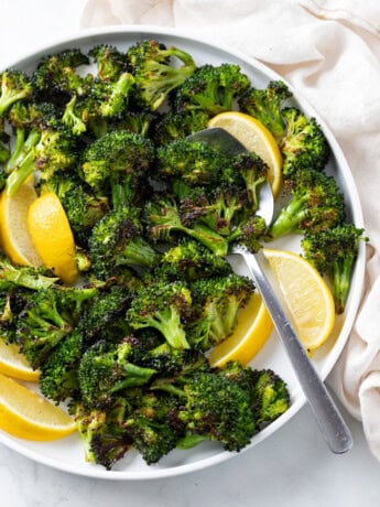 A white plate with roasted broccoli and slices of lemon with a spoon.