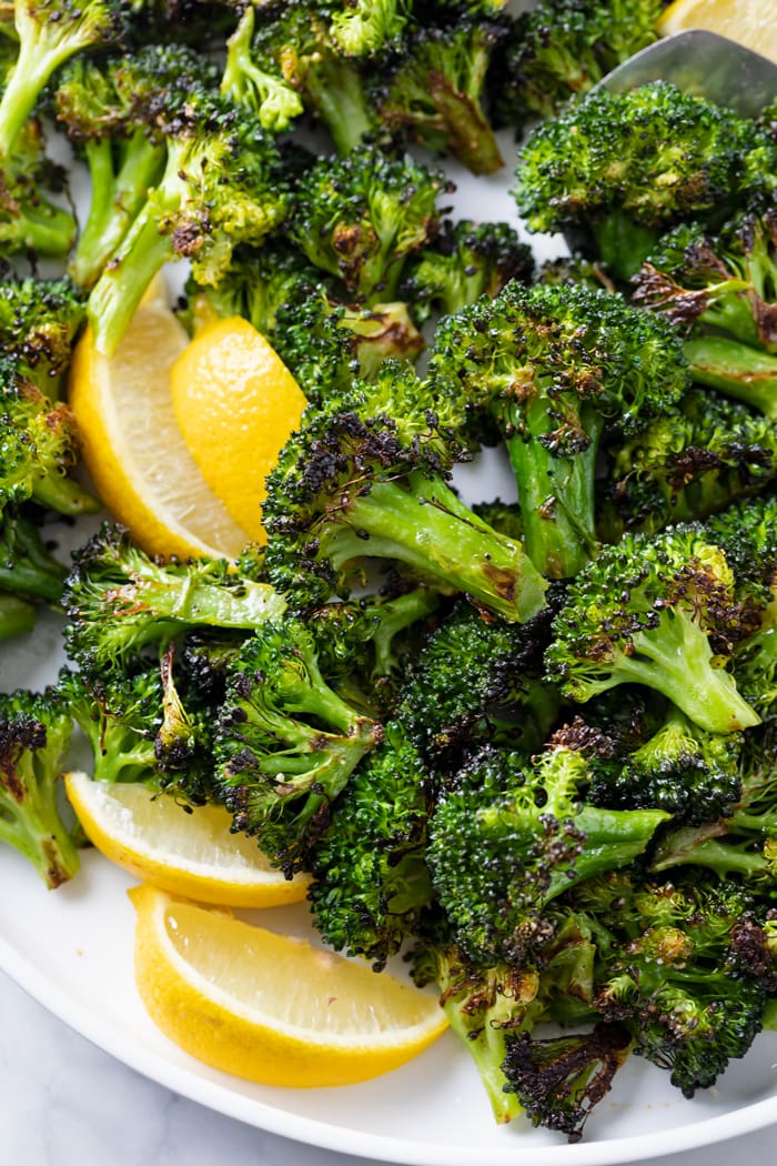Roasted Broccoli on a white plate with slices of fresh lemon.