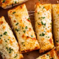 Slices of Cheesy Garlic Bread topped with cheese on a wooden cutting board.