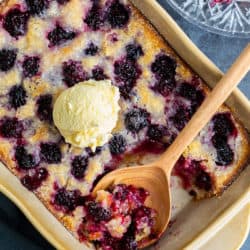 Blackberry Cobbler in a baking dish with a scoop of vanilla ice cream on top with a wooden spoon.