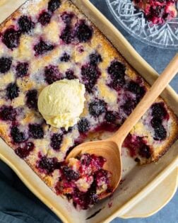 Blackberry Cobbler in a baking dish with a scoop of vanilla ice cream on top with a wooden spoon.