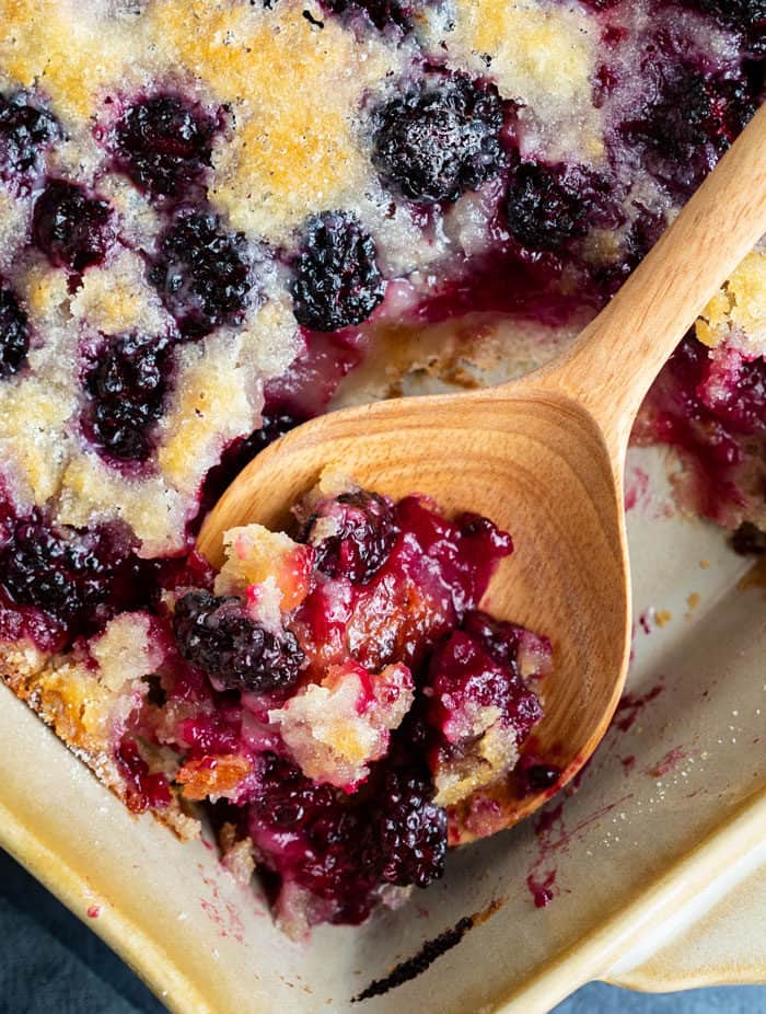 Close up view of a wooden spoon filled with juicy blackberry cobbler.