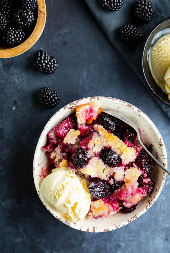 Overhead image of a bowl filled with Blackberry cobbler and a scoop of vanilla ice cream with a spoon.