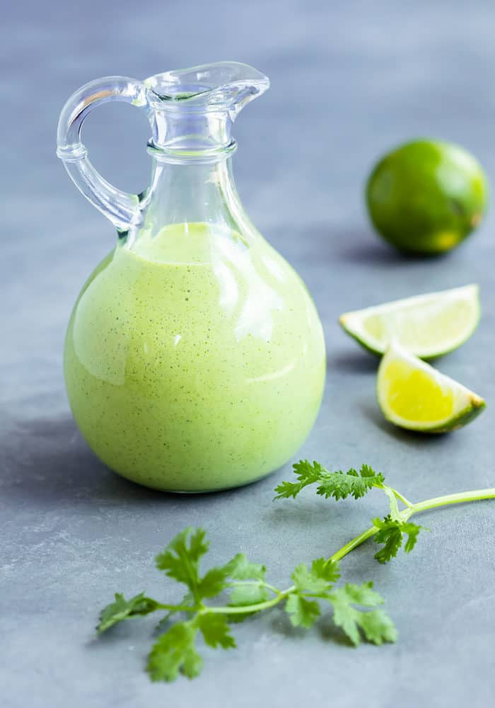 Cilantro Lime Dressing in a glass vessel with lime and cilantro next to it.