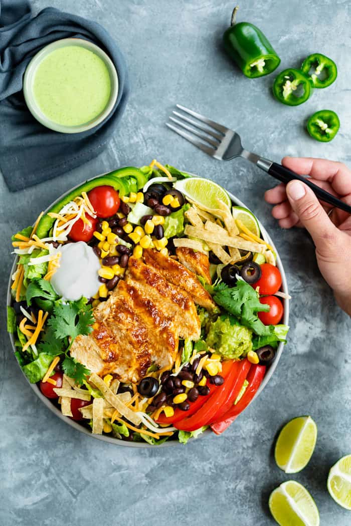 Southwest salad with chicken on top next to salad dressing and a hand holding a fork to eat it.