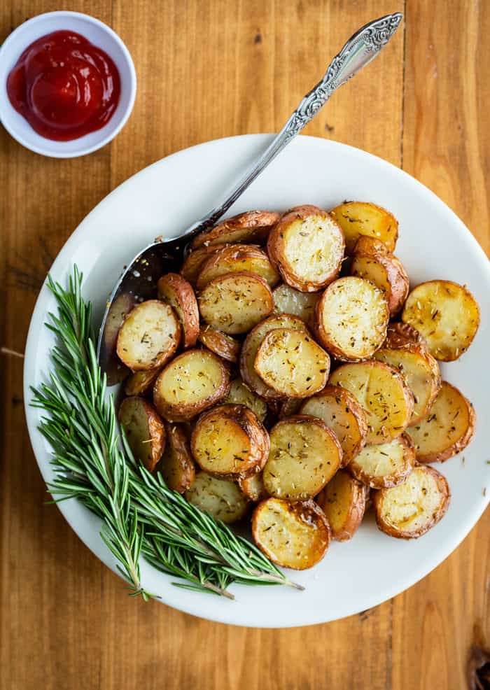Crispy Grilled Potatoes garnished with fresh rosemary in a white bowl on a wooden table.