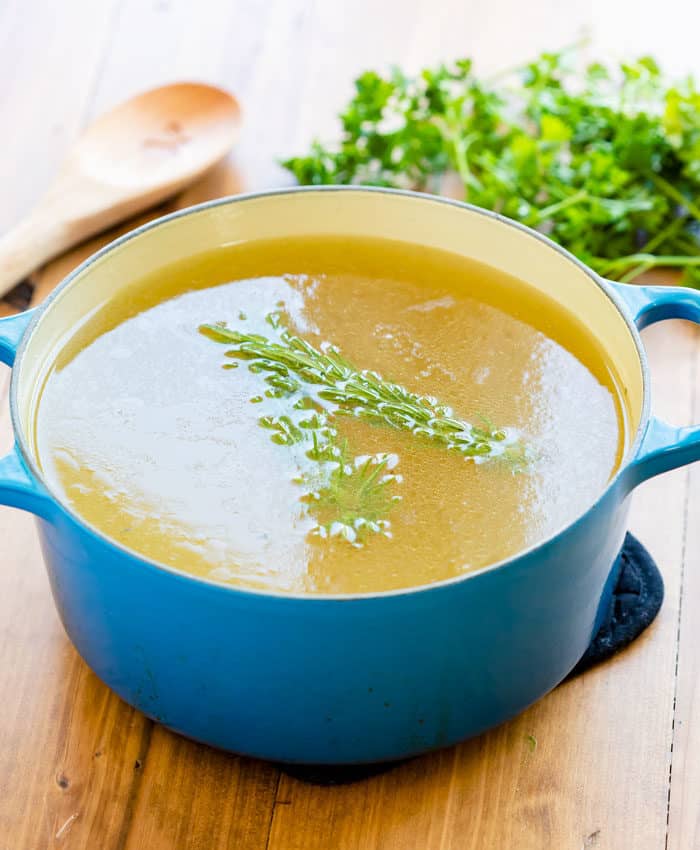Homemade chicken stock in a stock pot topped with fresh rosemary on a wooden surface.