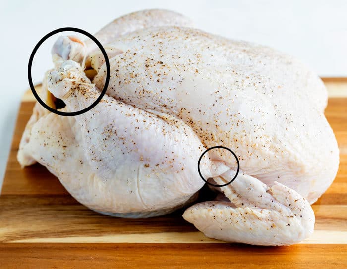 A raw chicken on a cutting board with circles showing how to tie the legs and tuck in the wings.