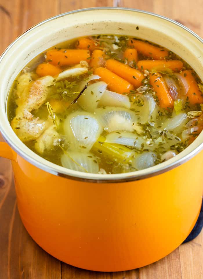 Large stock pot filled with vegetables and seasonings for homemade chicken stock.