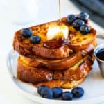 Syrup being poured over a stack of Alton Brown's french toast with blueberries.