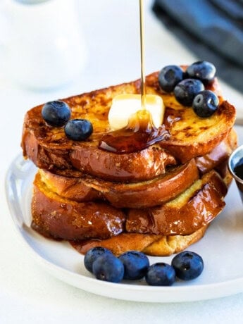 Syrup being poured over a stack of Alton Brown's french toast with blueberries.