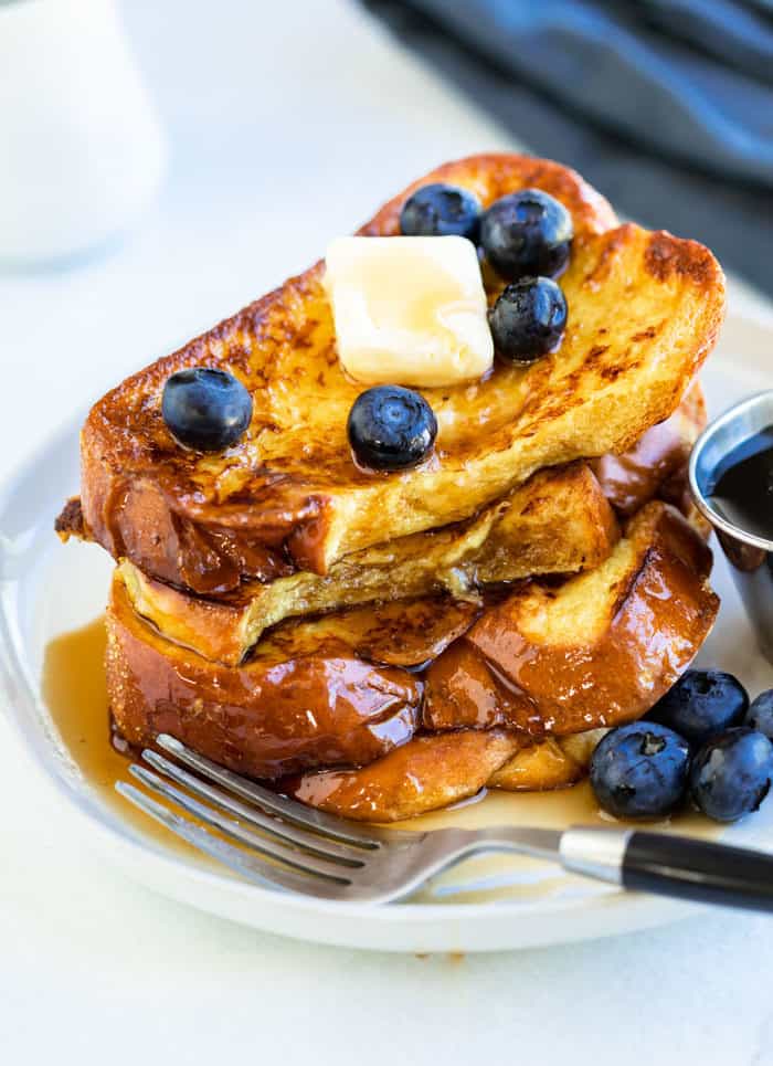A stack of french toast with a fork sitting next to it on a white plate.