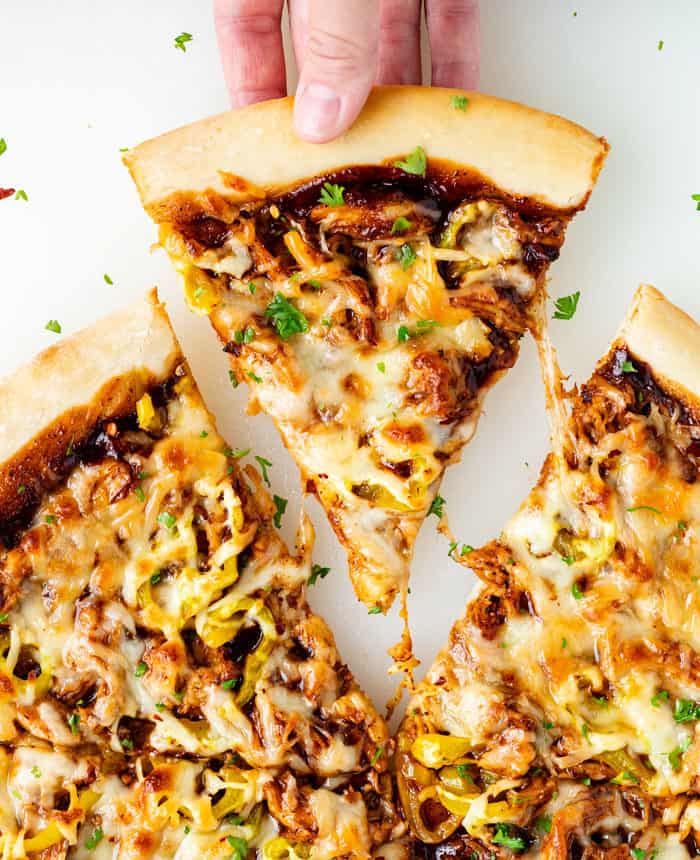 A slice of BBQ Chicken Pizza being pulled out from the pizza pie and topped with parsley.