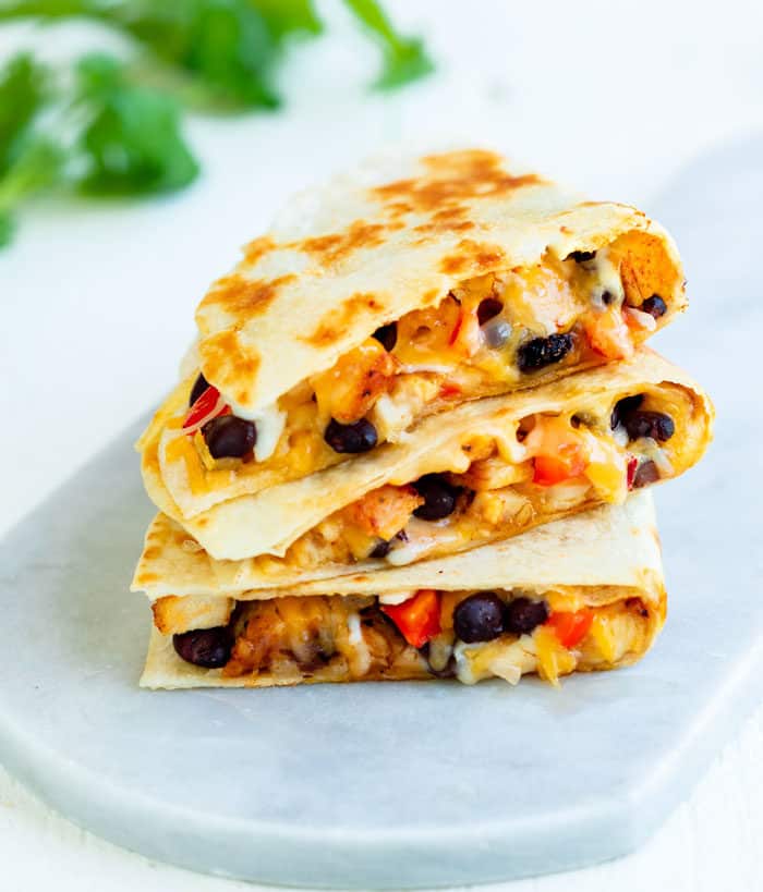 Crispy chicken quesadillas filled with black beans and melted cheese on a white surface.