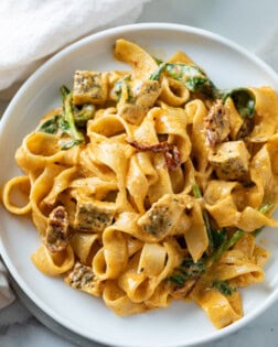 A white plate topped with creamy Tuscan Chicken Pasta with spinach and chicken.