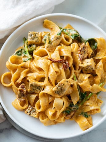 A white plate topped with creamy Tuscan Chicken Pasta with spinach and chicken.