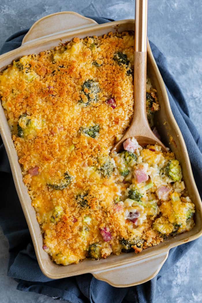 a casserole dish filled with ham casserole with a wooden spoon scooping some of it out.