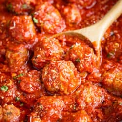A pot filled with Italian Meatballs with a wooden spoon.