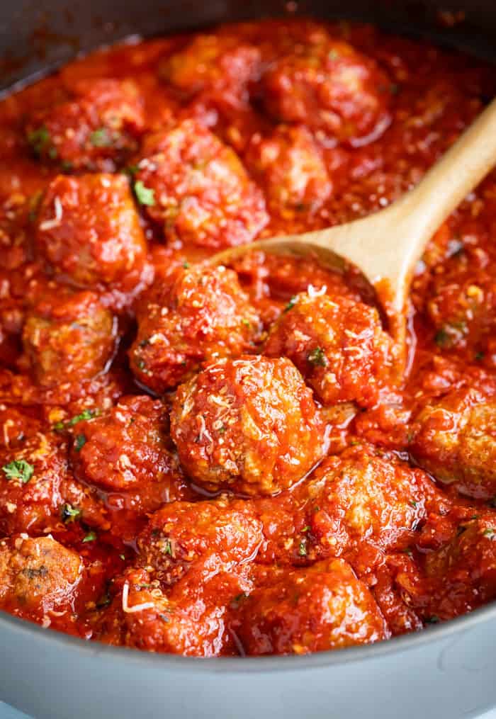A skillet full of meatballs and marinara sauce with a wooden spoon scooping them up.