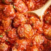 Italian meatballs sprinkled with Parmesan cheese being scooped by a wooden spoon.