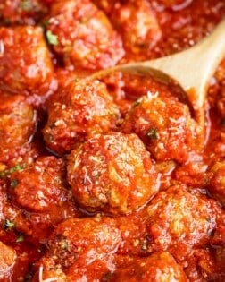 Italian meatballs sprinkled with Parmesan cheese being scooped by a wooden spoon.