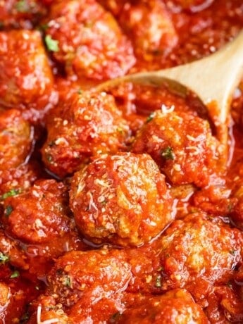 Italian meatballs sprinkled with Parmesan cheese being scooped by a wooden spoon.