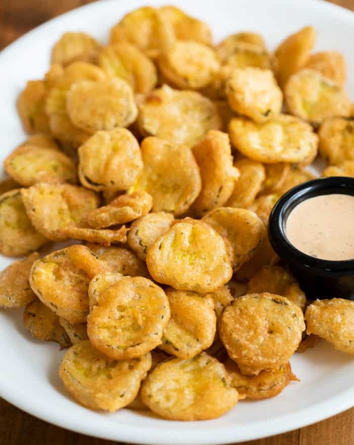 A white platter full of golden fried pickles and a ramekin of dipping sauce.