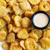 A plate full of crispy fried pickles with dipping sauce.