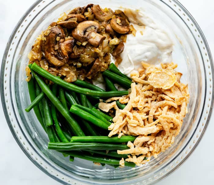 A glass bowl filled with ingredients needed to make green bean casserole.