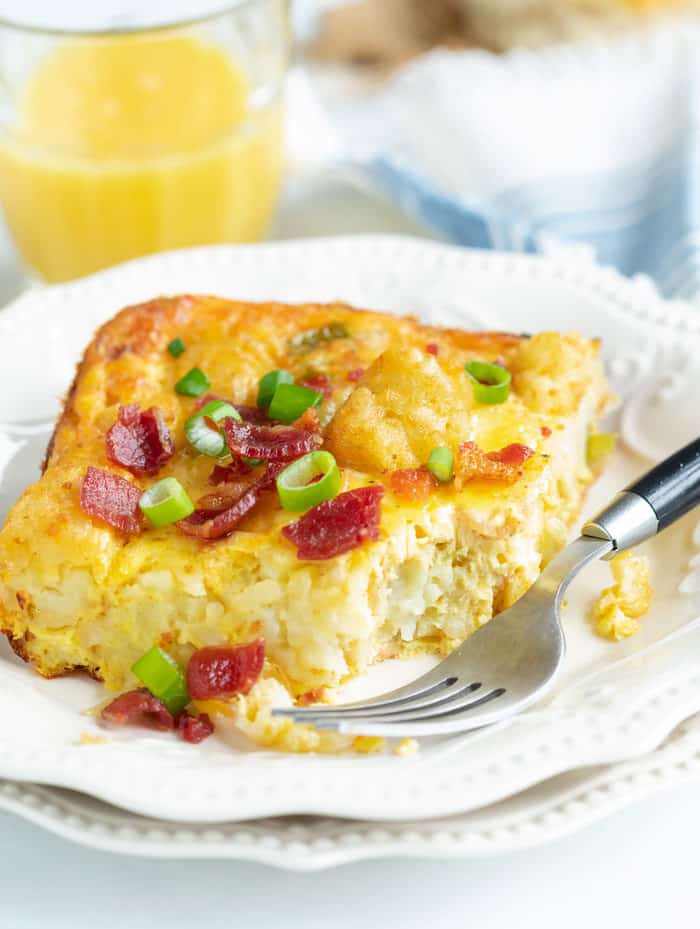 A piece of tater tot breakfast casserole with a bite taken out of it on a white plate with a fork.
