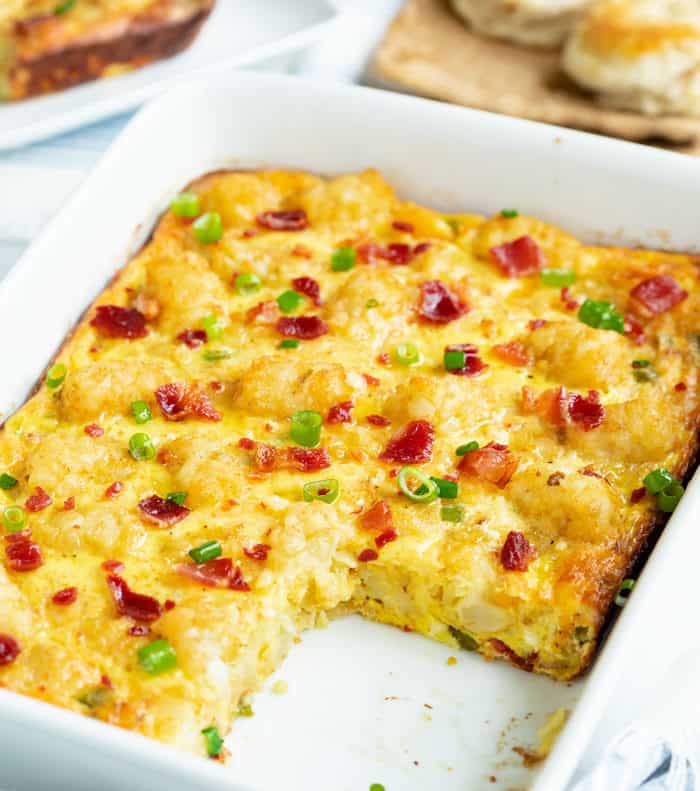 Tater tot breakfast casserole in a white casserole dish with a slice taken out of it.